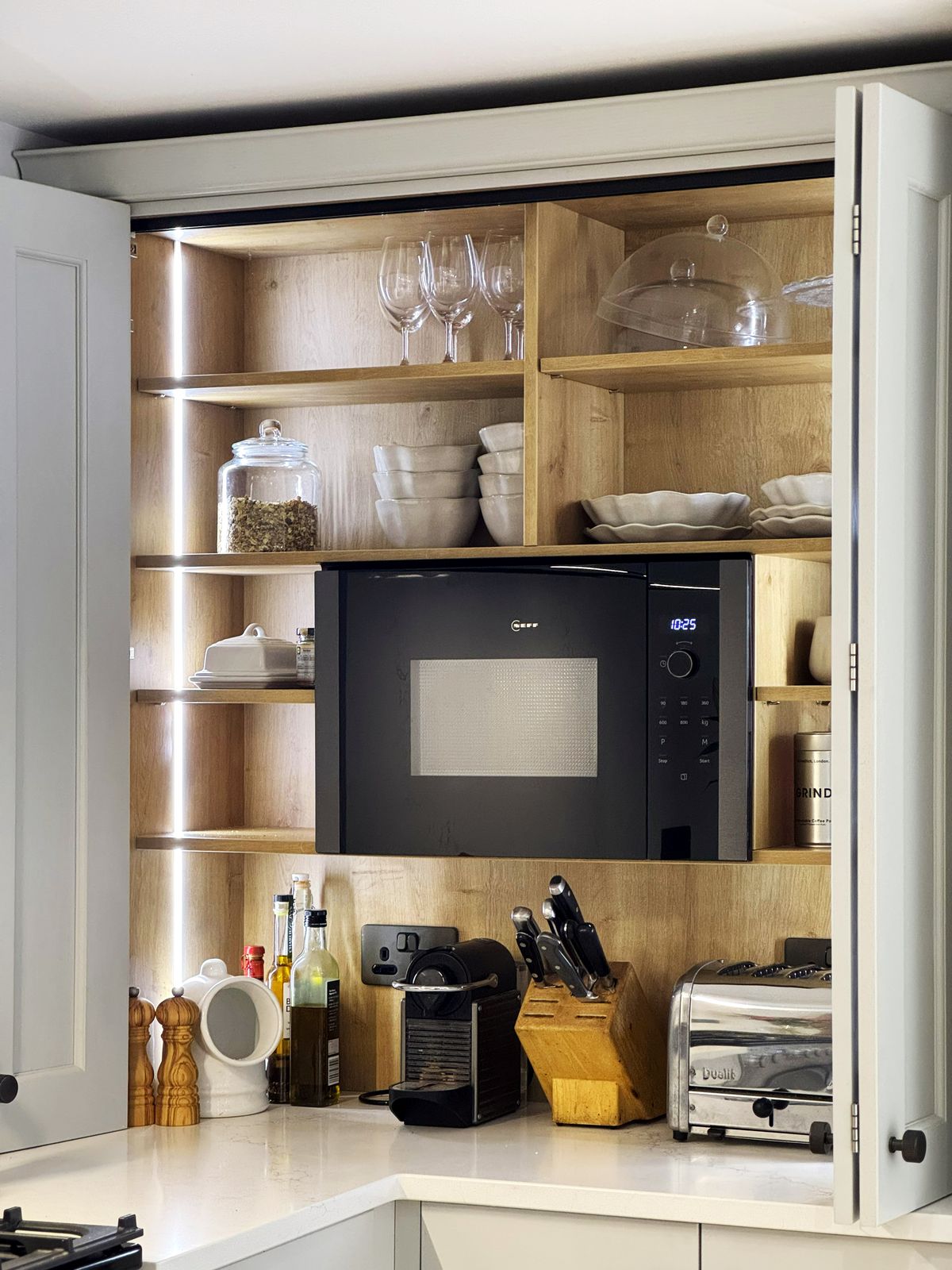 A breakfast cupboard with lit oak shelves, a microwave and a coffee machine