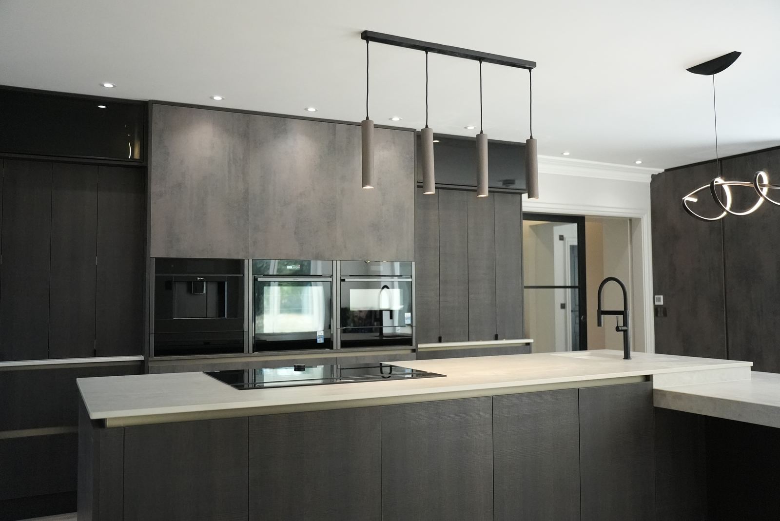 Dark oak-effect kitchen with a stepped Dekton island, pendant lights and a bank of built-in ovens