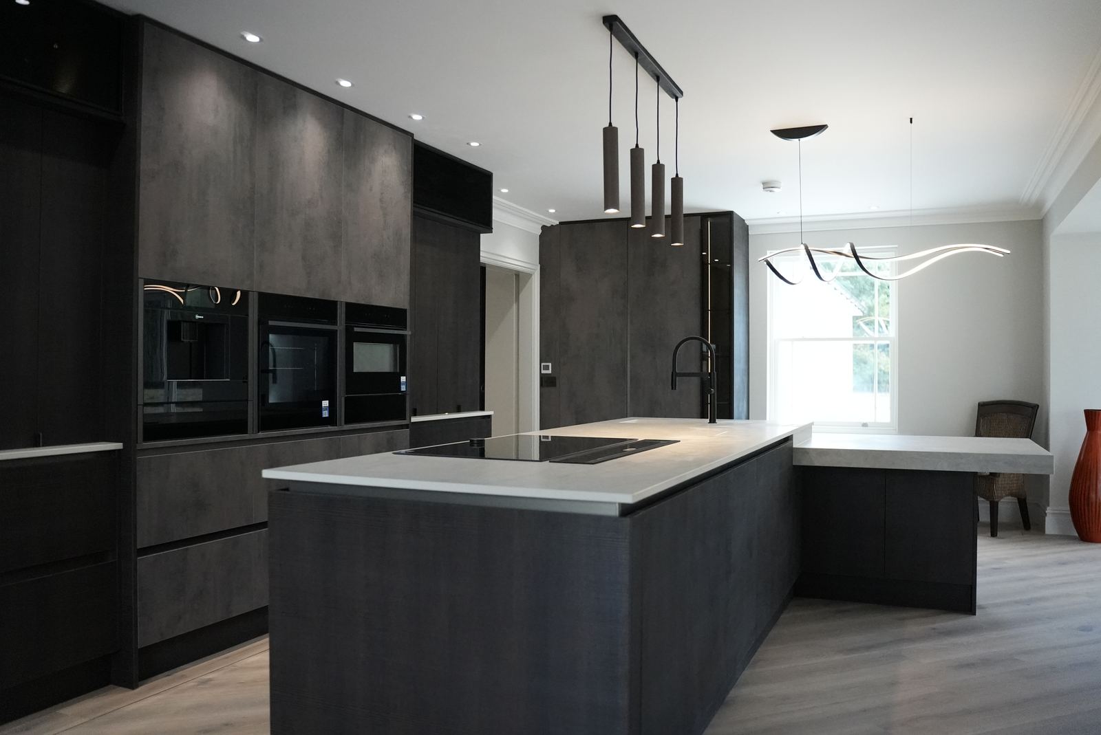 Island hob with downdraft extraction in front of tall dark units with built-in ovens and warming drawers