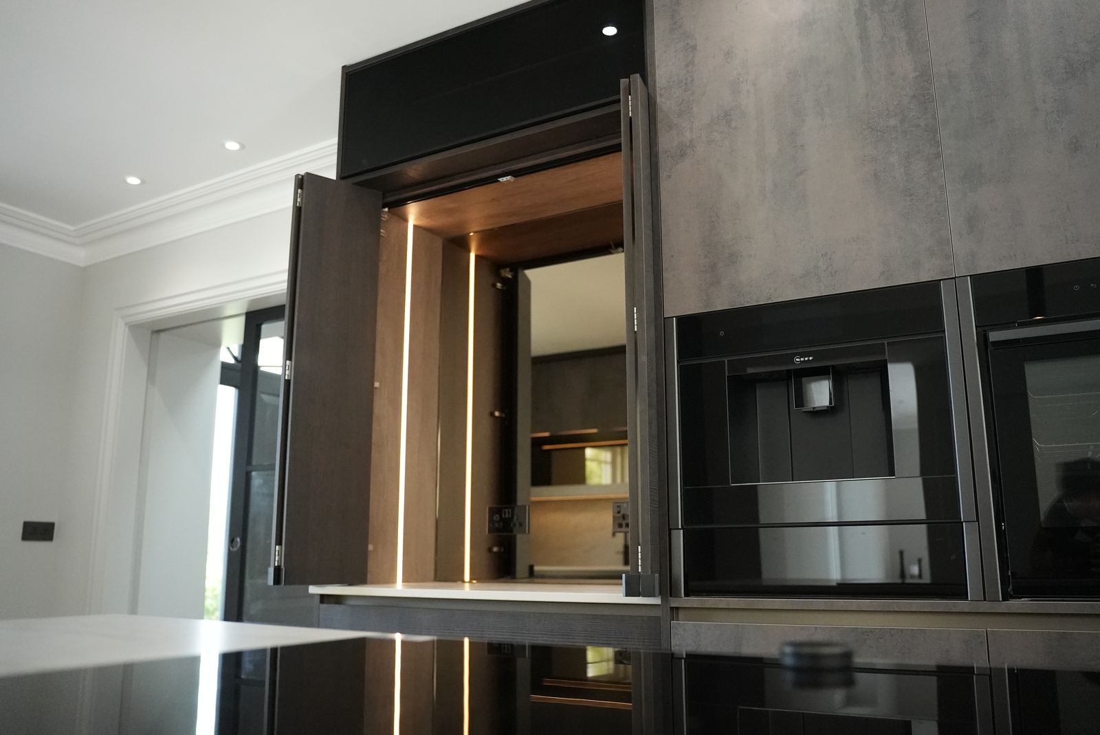 Open pocket-door pantry cabinet with lit timber interior beside a built-in coffee machine