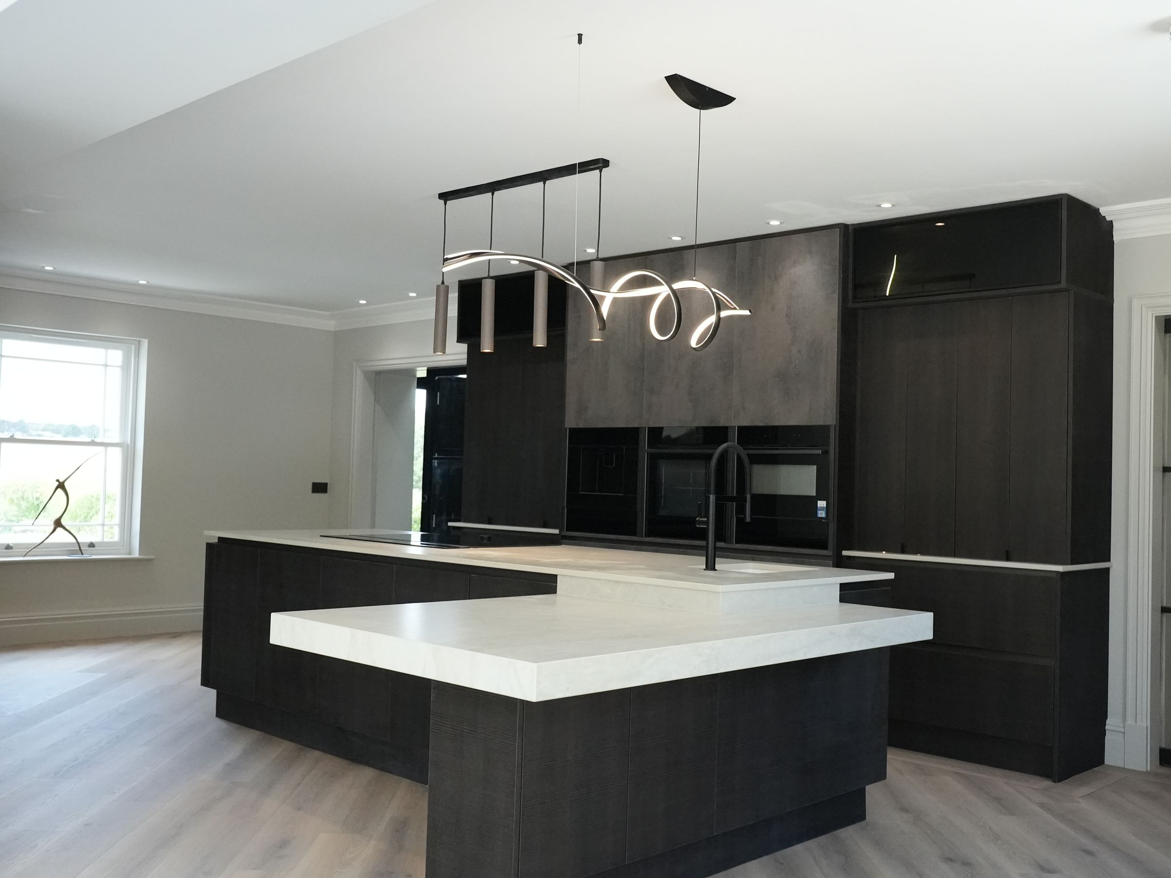 A dark wood kitchen with a two-level white island and a spiral pendant light