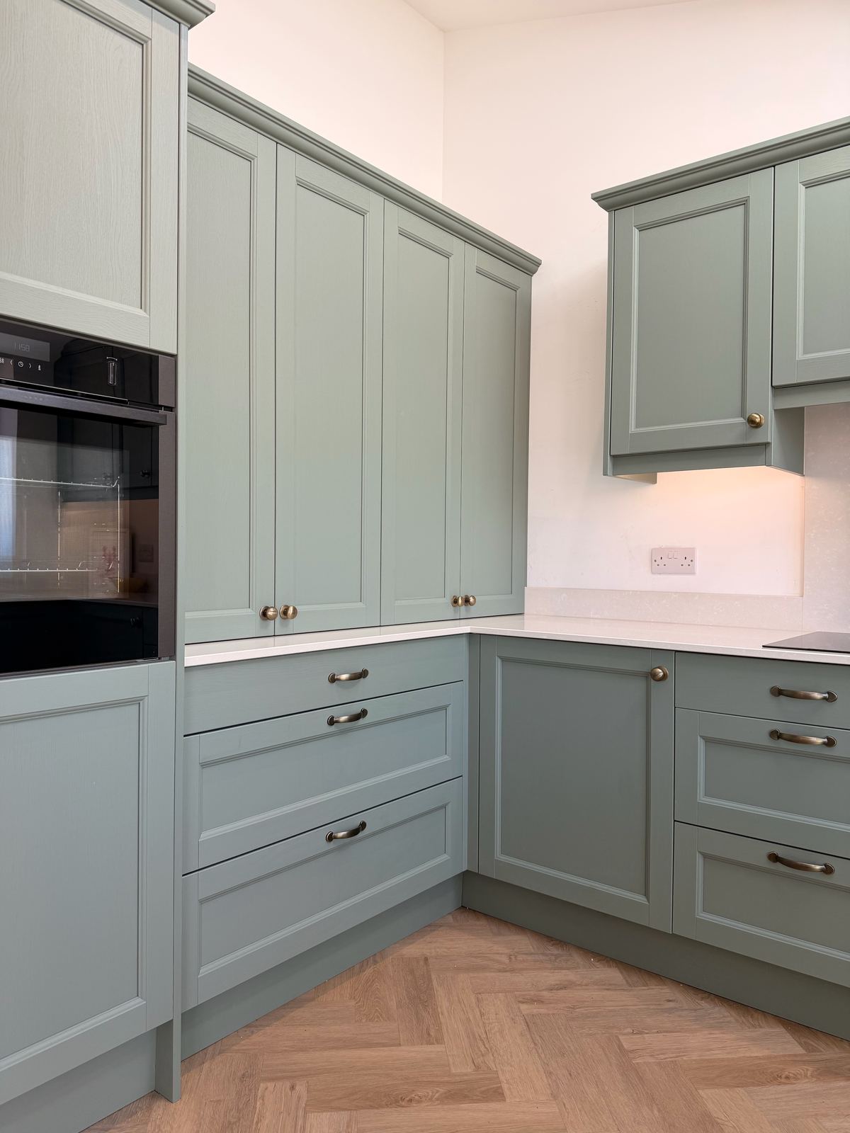 A Reed Green shaker kitchen with a peninsula and brass pendants