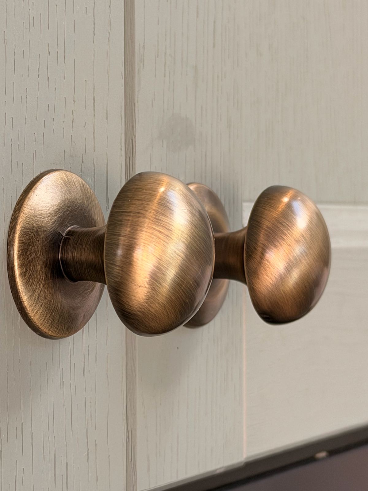 Close-up of aged brass cabinet knobs on a painted woodgrain door