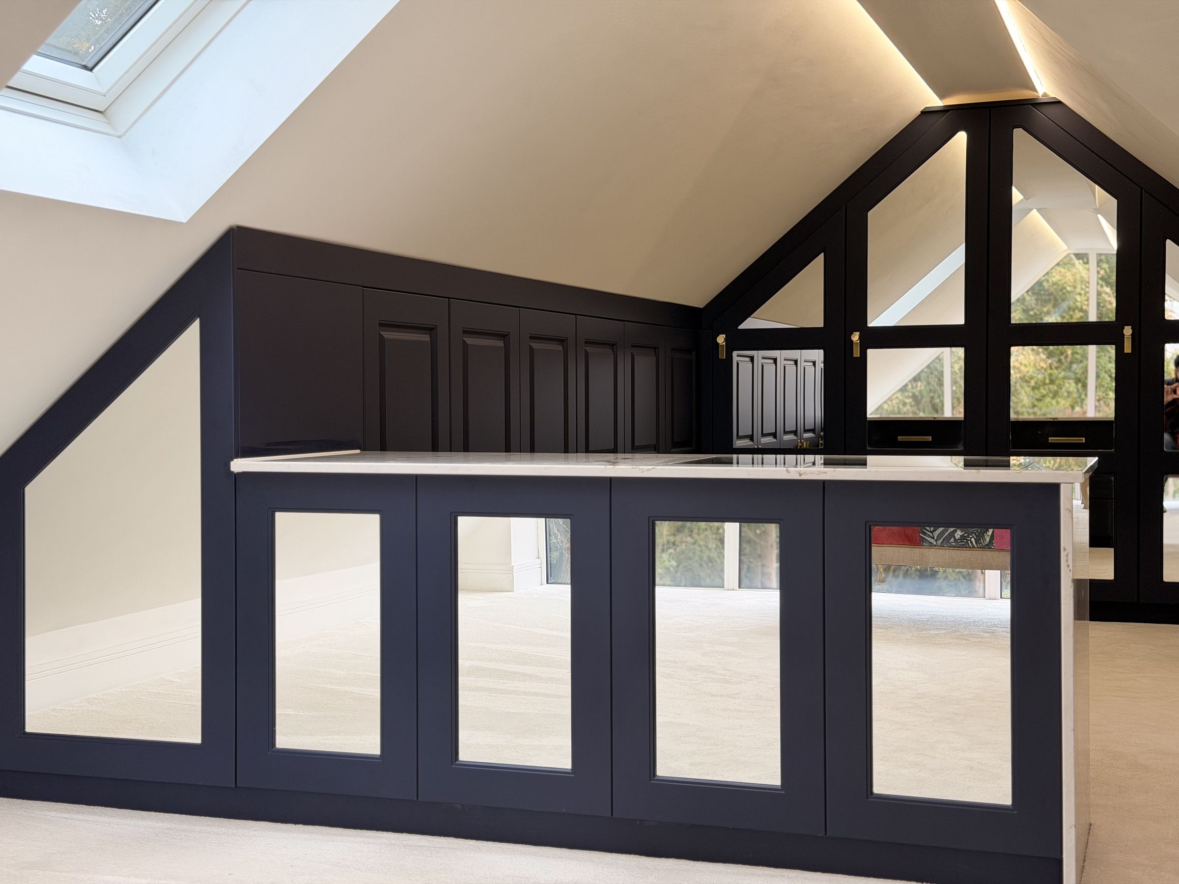 A navy loft dressing room with a mirrored island and glazed doors under the gable