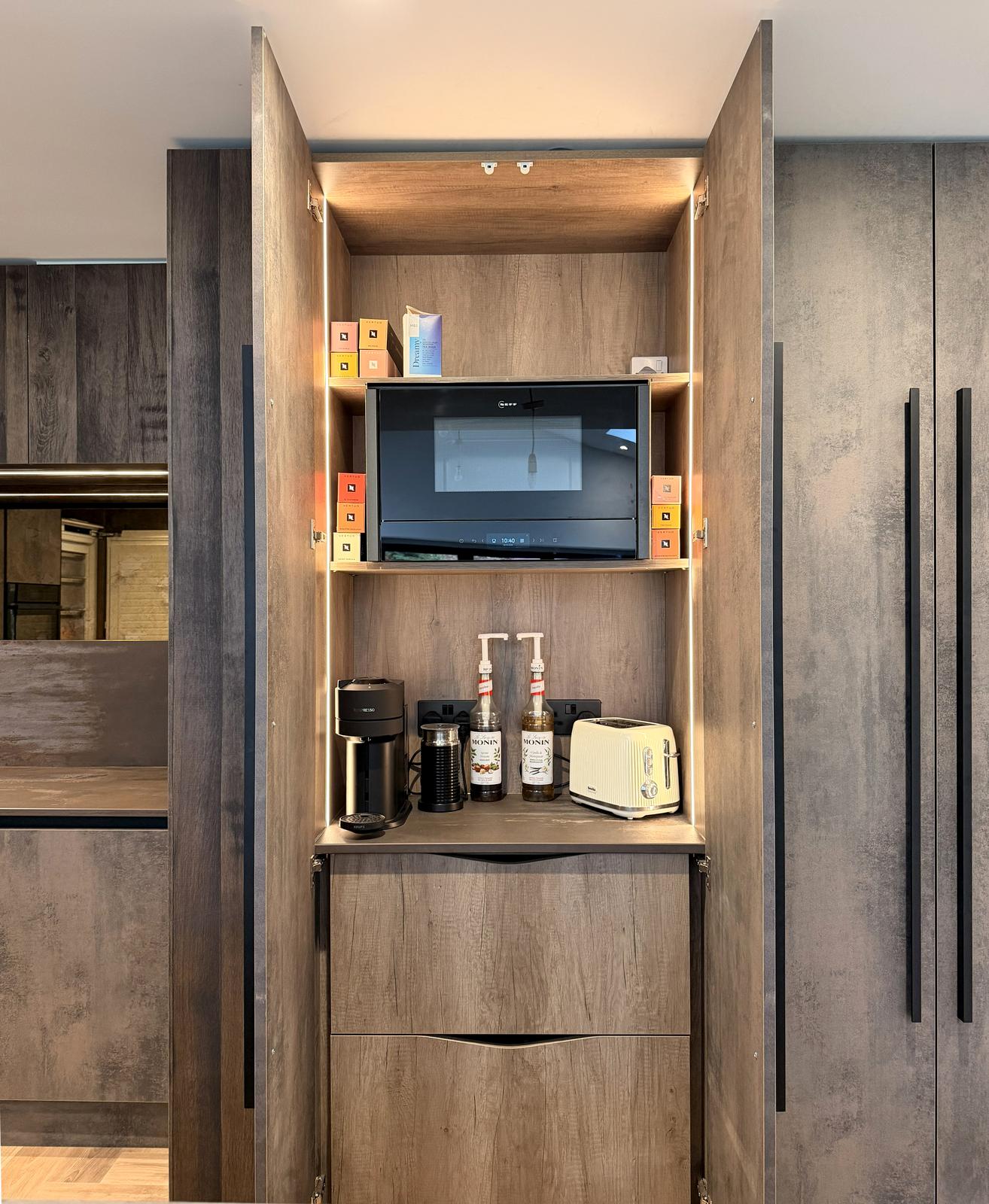 Tall pantry cupboard open with lit shelving, microwave and a coffee station