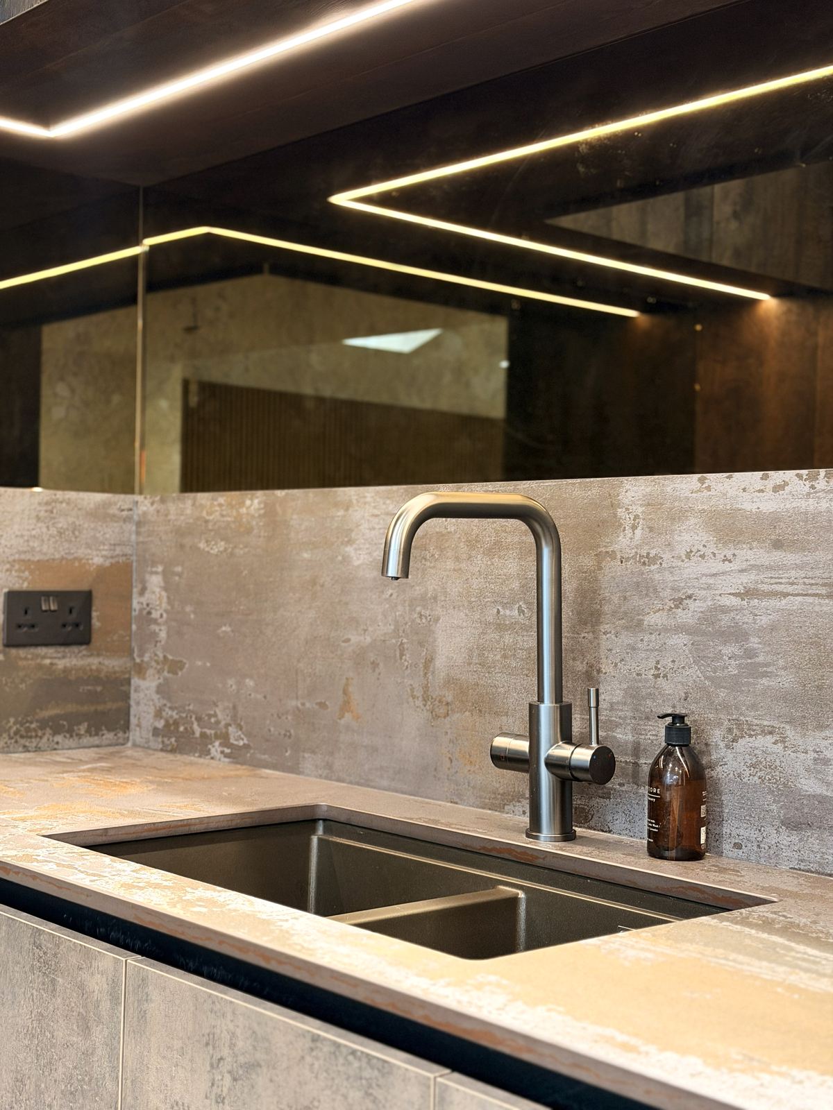 Undermount sink with a brushed tap against a stone-effect splashback with LED lighting