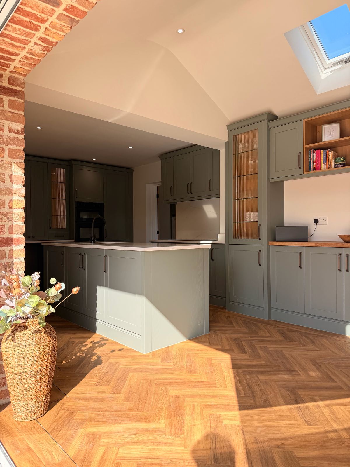 Sage green shaker kitchen extension with a brick arch, skylight and herringbone floor