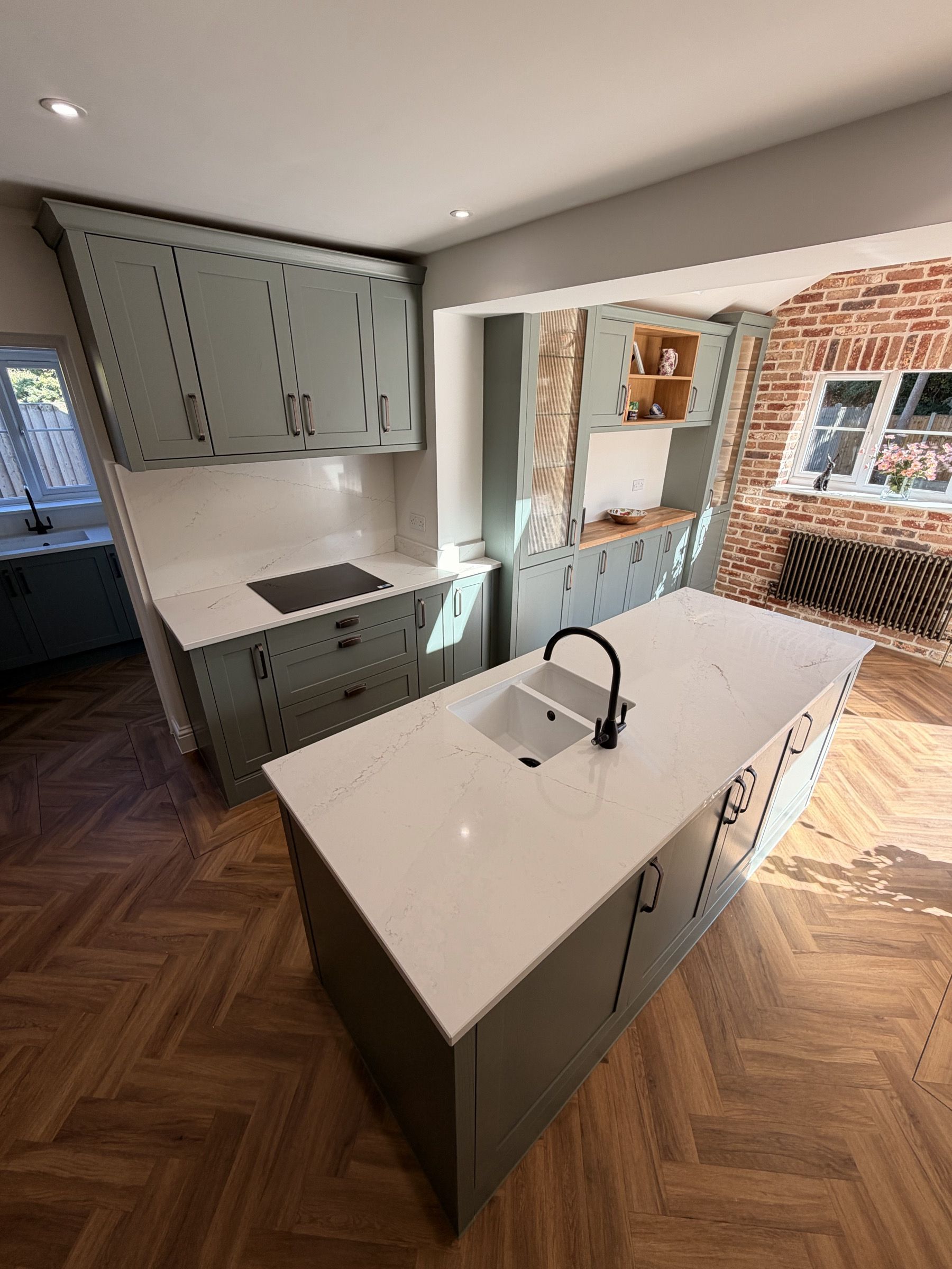 A sage green shaker kitchen made by CEK, with a brick arch and oak shelves